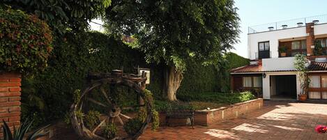 A courtyard with a large water wheel, brick pathway, and a modern building with a balcony.