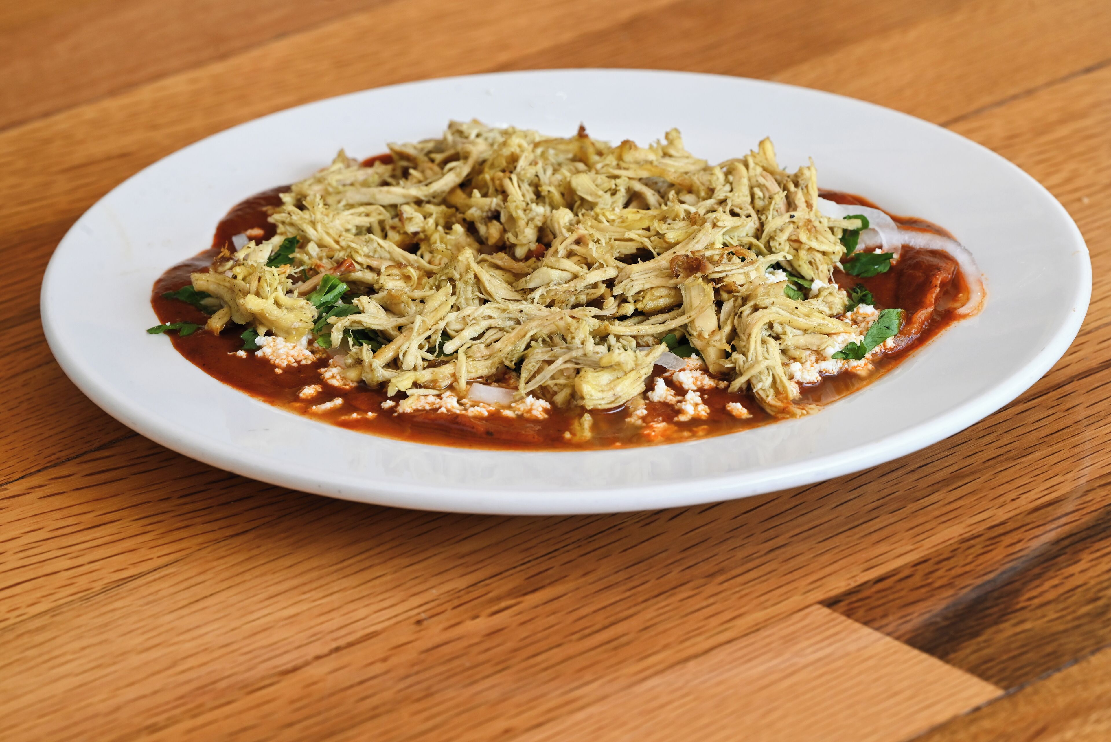 A white plate with shredded chicken, garnished with herbs, on a wooden table.