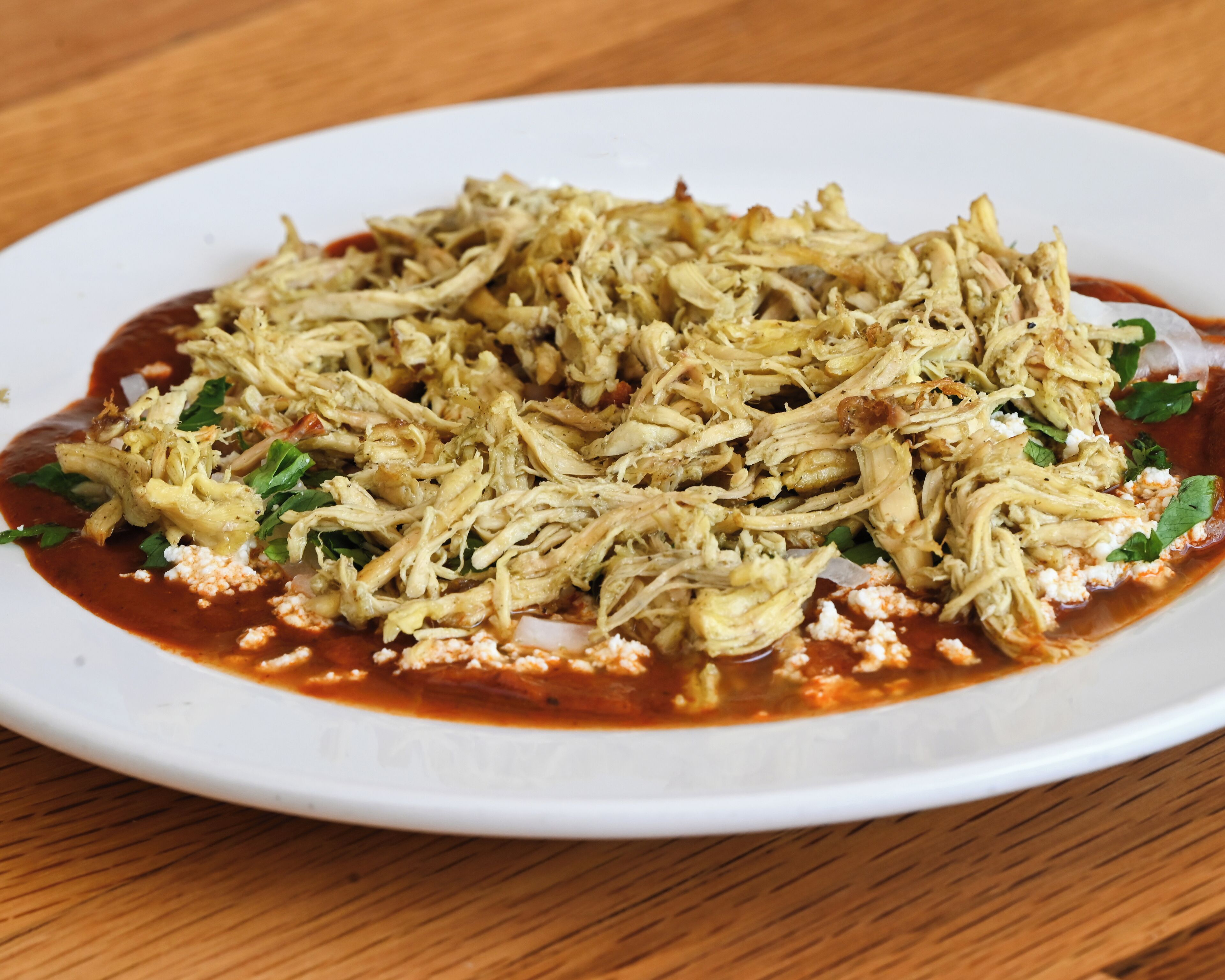 A plate of shredded chicken with a red sauce and garnished with herbs.