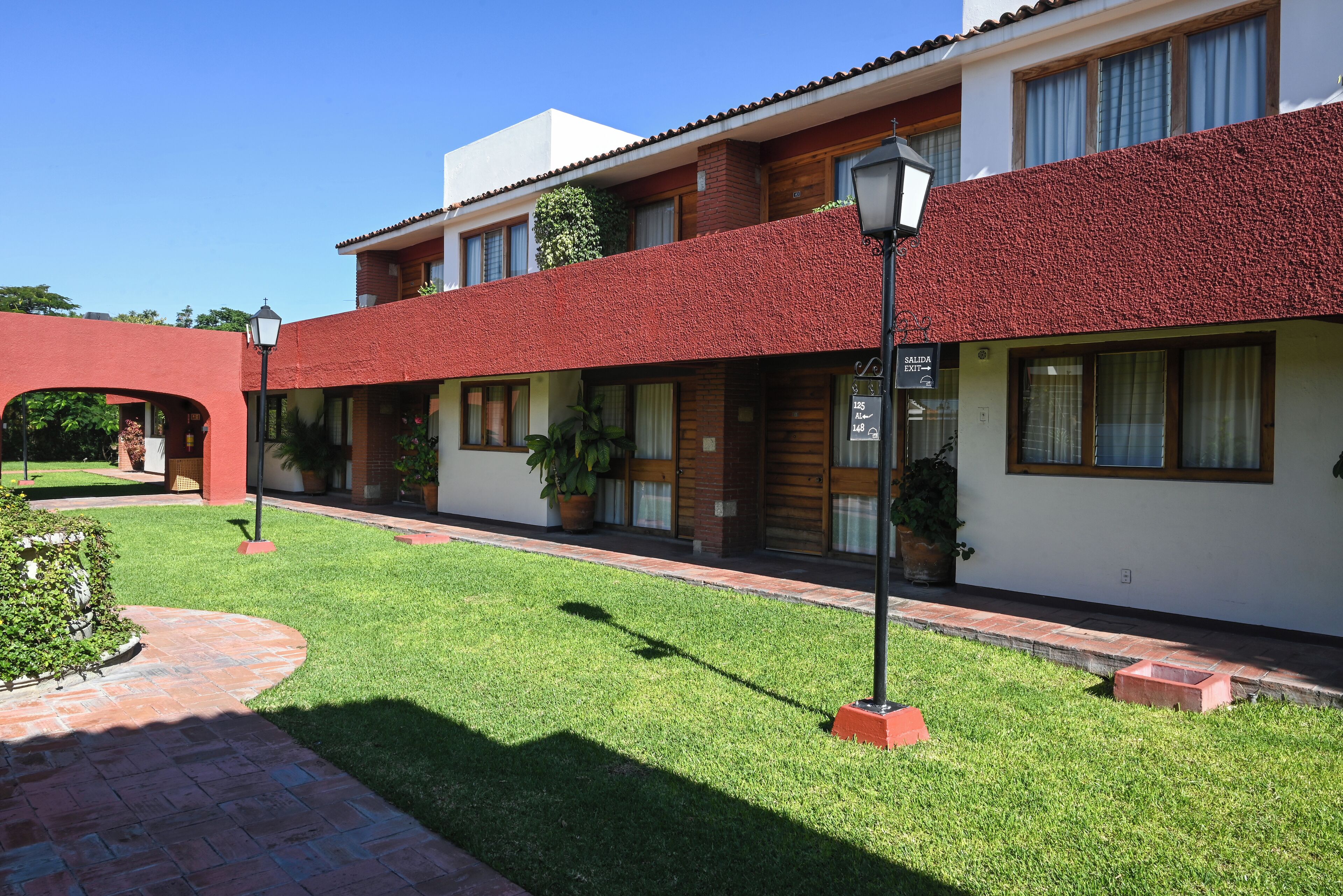 A two-story building with a red-tiled roof, a brick facade, and a small garden area with a pathway.