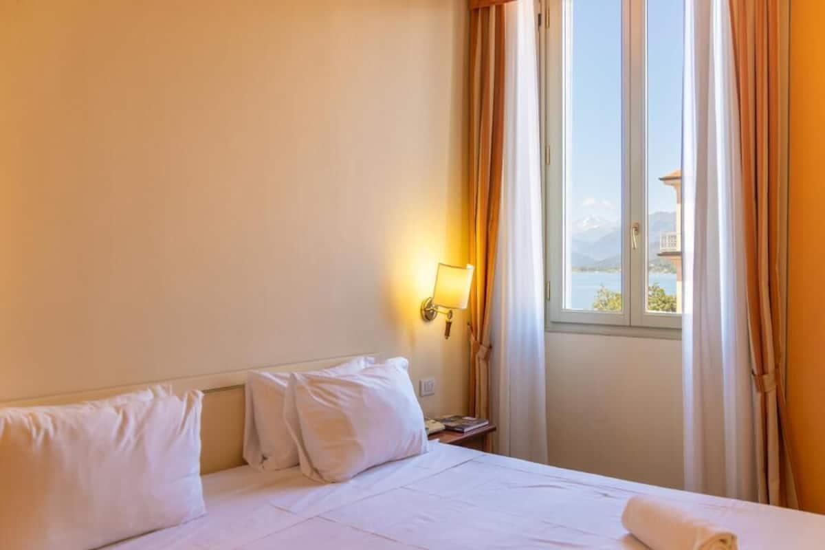 A hotel room with a bed, a nightstand, a lamp, and a window with curtains.