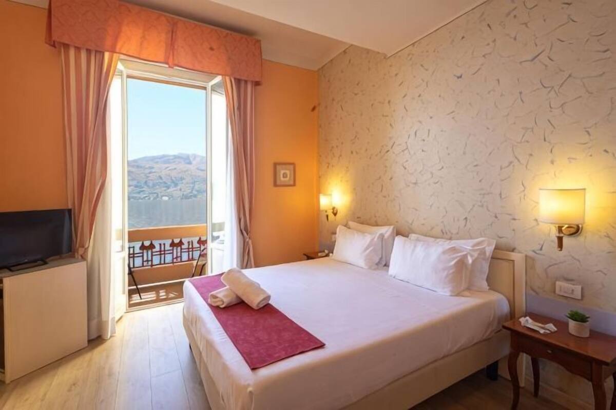 A hotel room with a bed, a TV, a balcony with curtains, and a wall with a bird pattern.