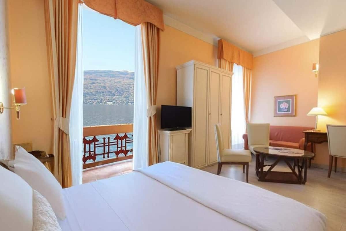 A hotel room with a bed, a television, a desk, and a chair. There is a view of a body of water and hills in the background.