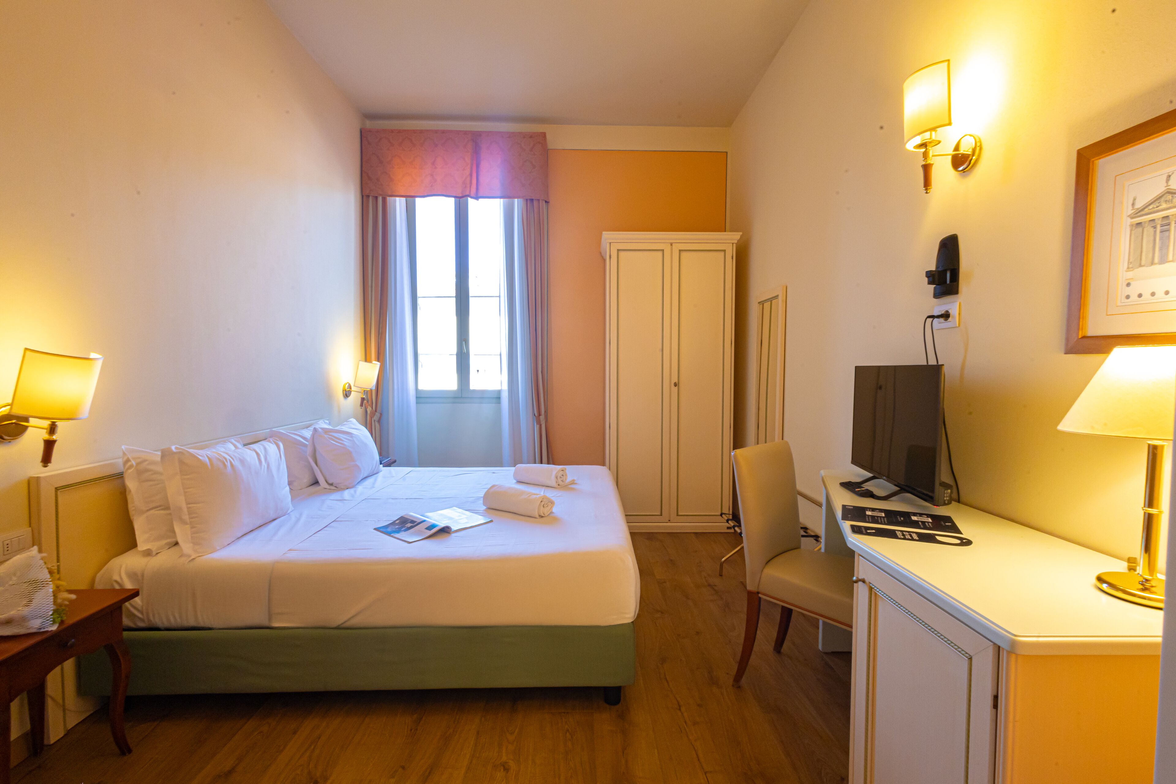 Habitación de hotel con cama, escritorio, silla, televisor y ventana con cortinas.