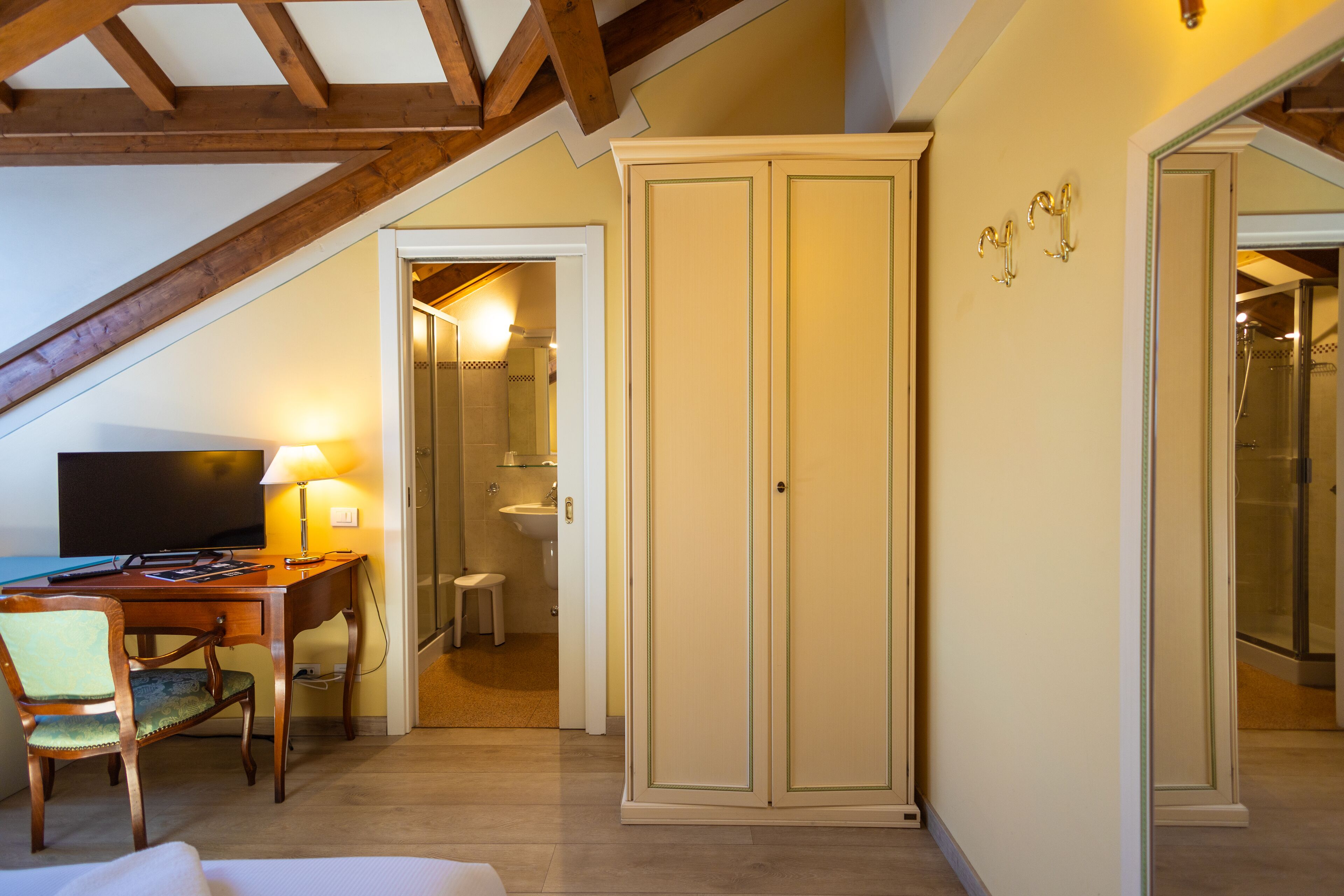 A hotel room with a wooden desk, a television, a lamp, a wardrobe, and a bathroom visible through an open door.