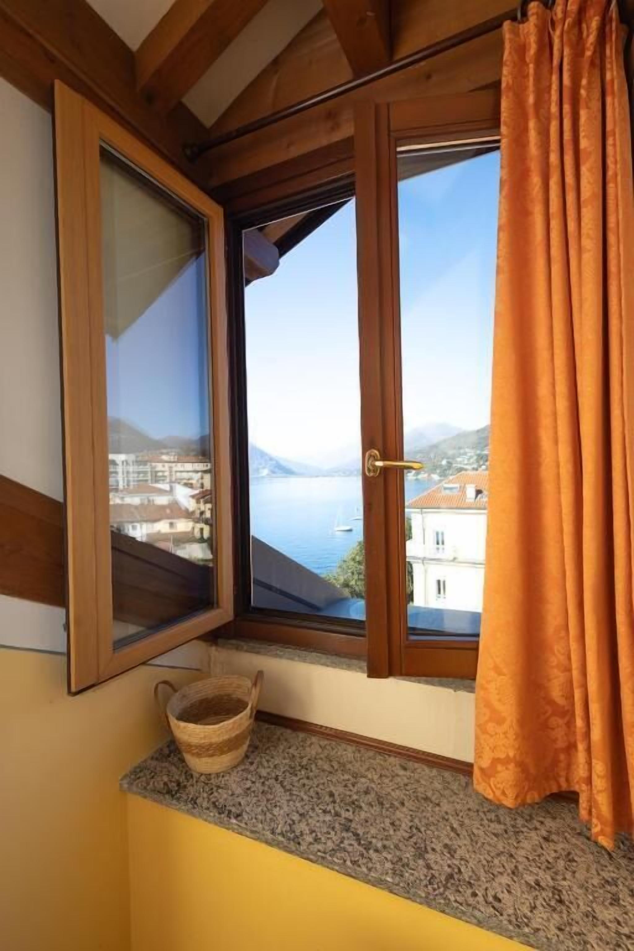 A room with a window overlooking a body of water and buildings, a wooden ceiling, and a basket on the windowsill.