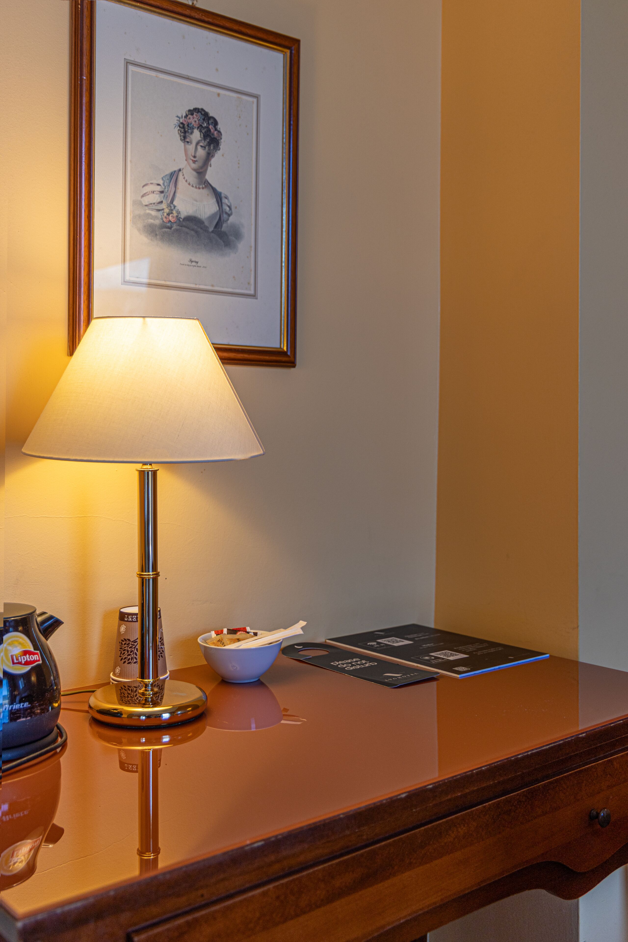 A wooden desk with a lamp, a framed picture, a bowl of cereal, and a coffee maker.