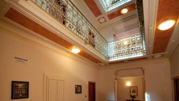 Un ambiente spazioso con un'imponente scalinata, ringhiere in metallo decorate e un soffitto alto con lucernari.