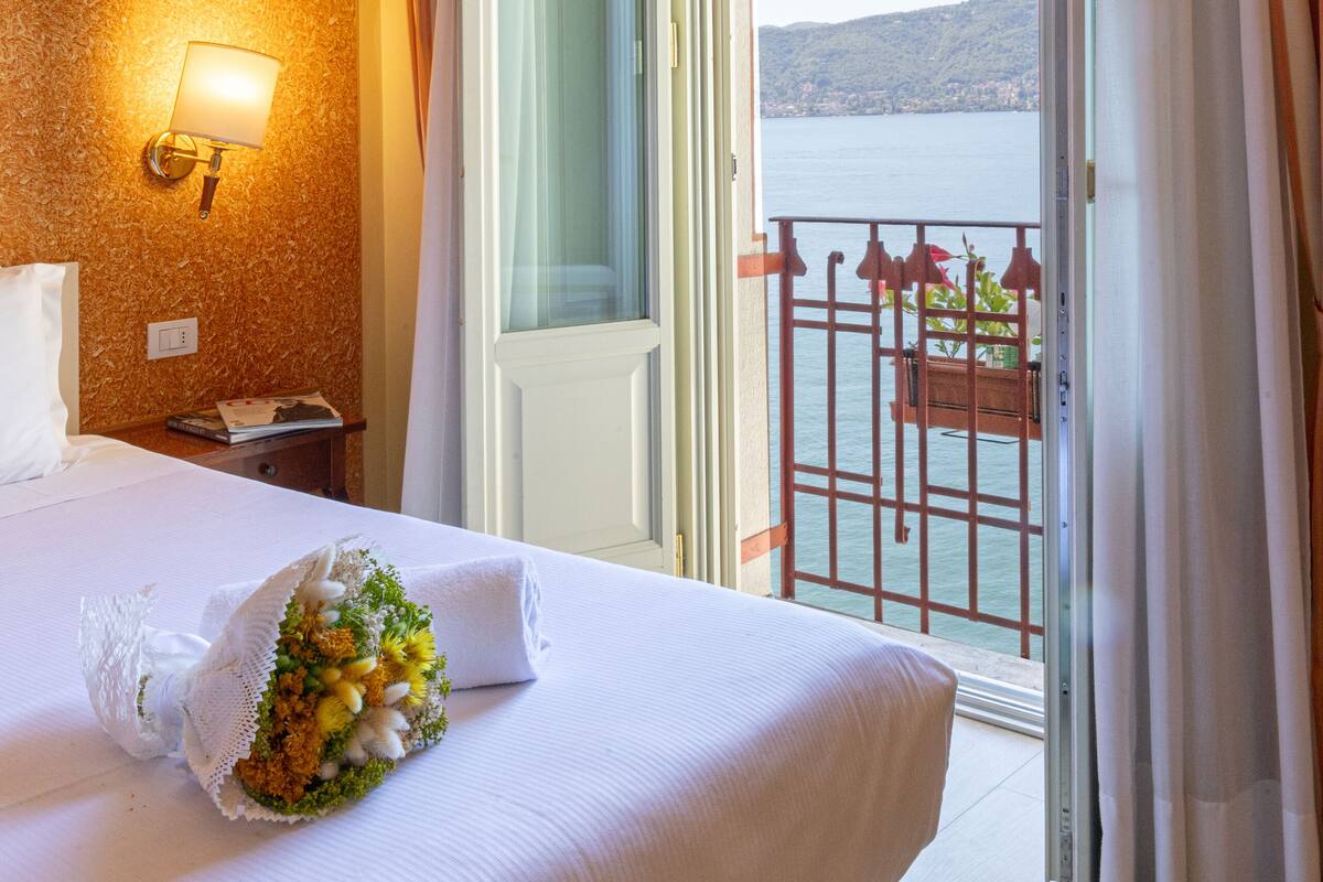 A hotel room with a bed, a nightstand, a lamp, and a view of the sea through a balcony.