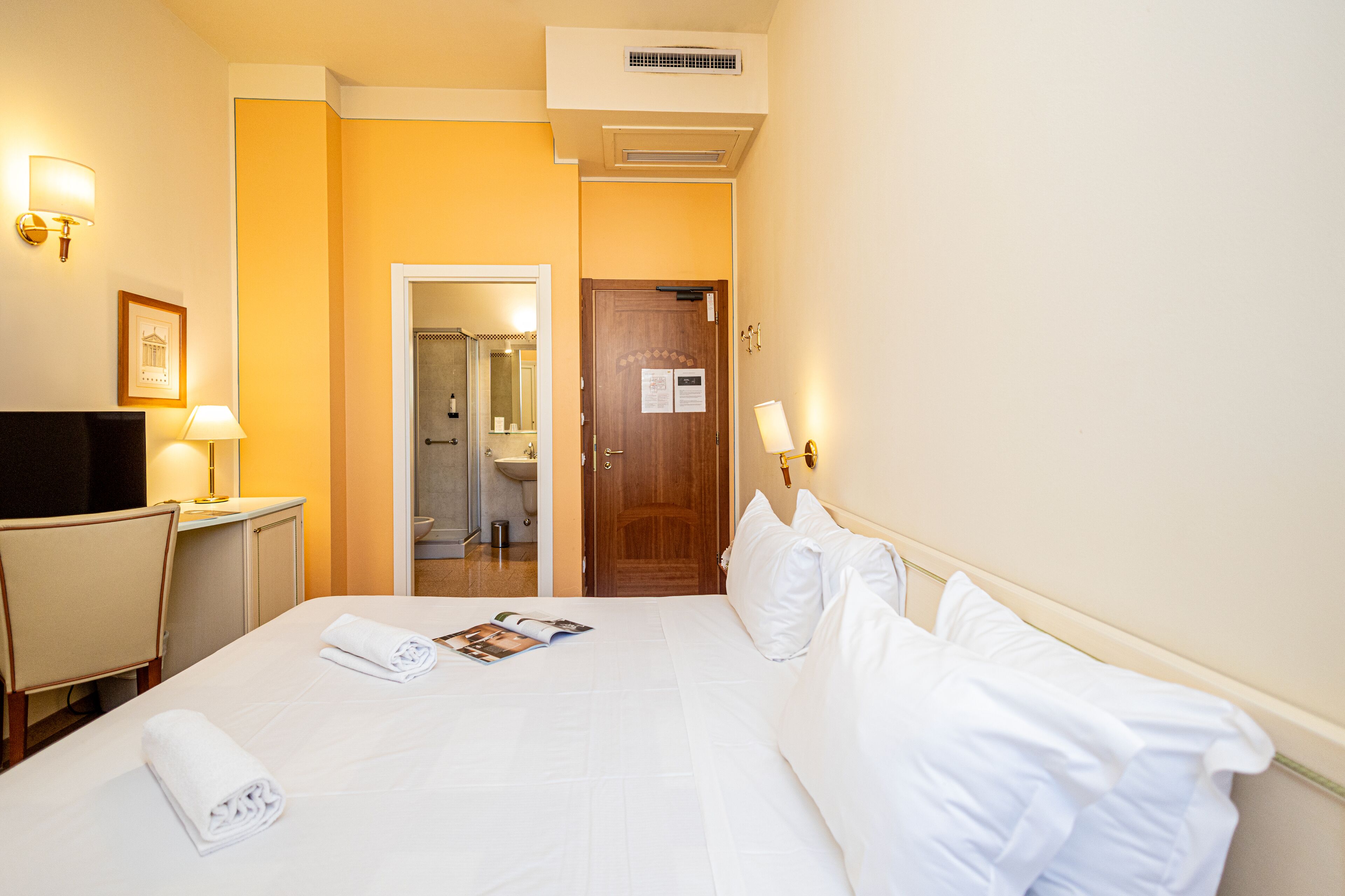 Habitación de hotel con cama, escritorio, silla, televisión y baño visible a través de una puerta abierta.