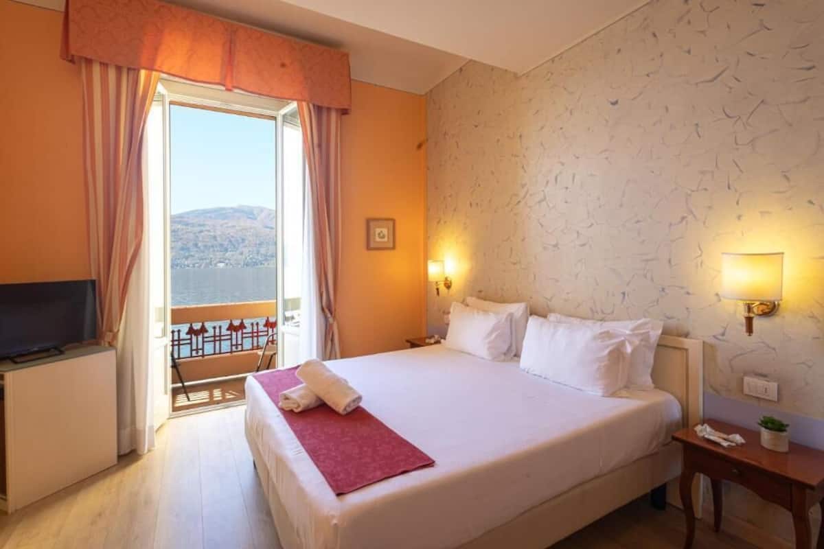 A hotel room with a large bed, a TV, a balcony with a view, and a patterned wall.