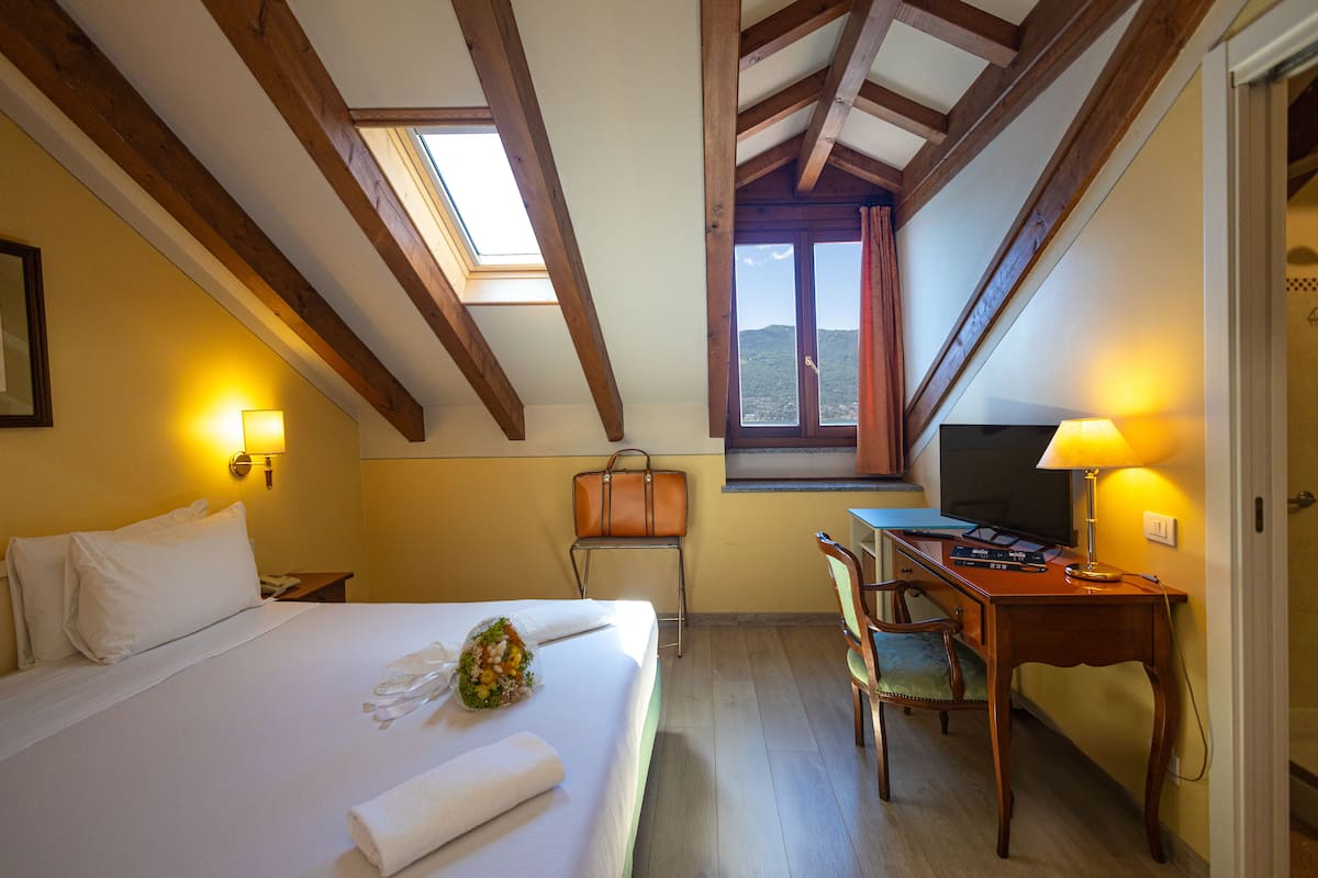 A hotel room with a bed, a desk, a chair, a TV, and a window with a view.