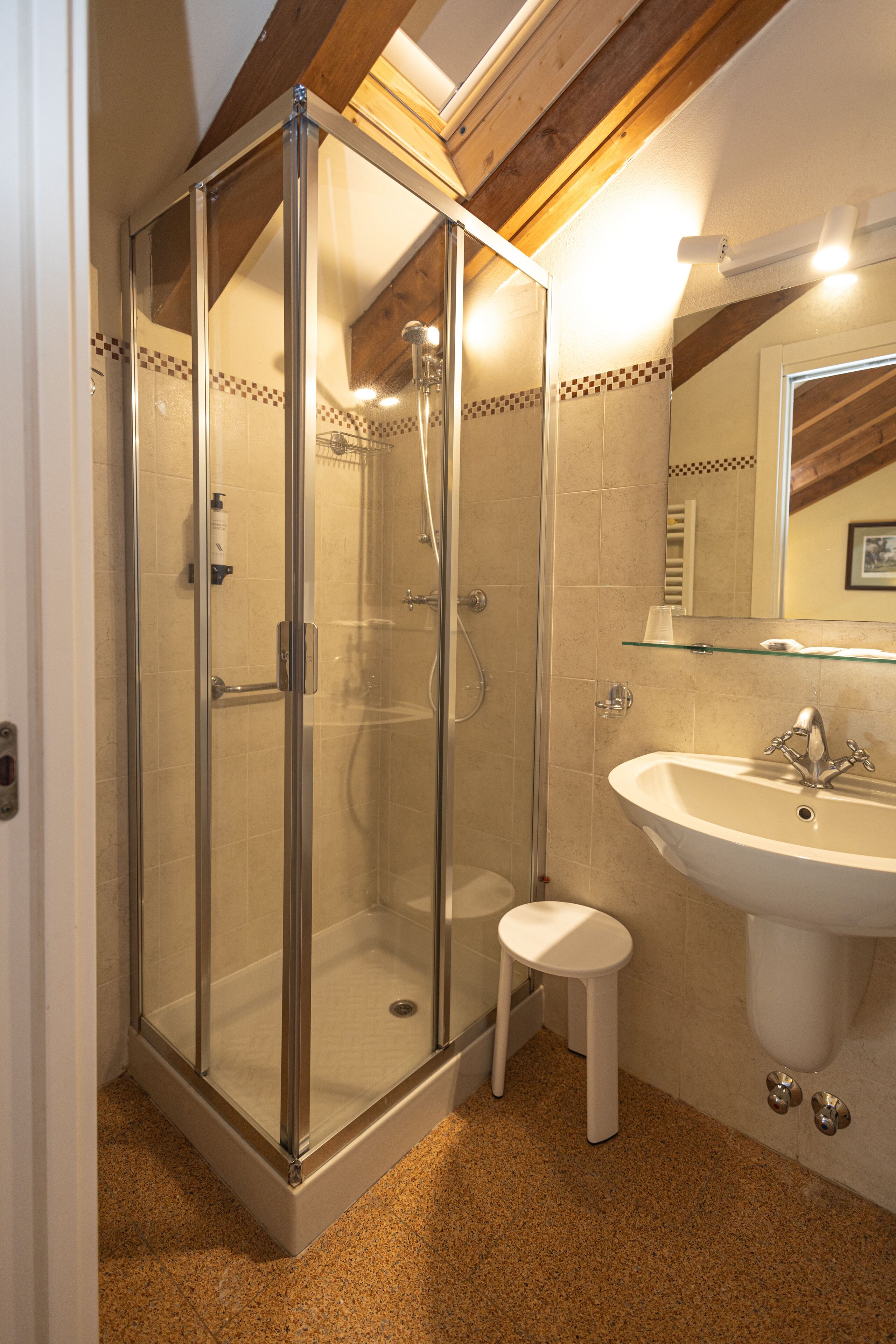 A bathroom with a glass-enclosed shower, a sink, and a small stool.