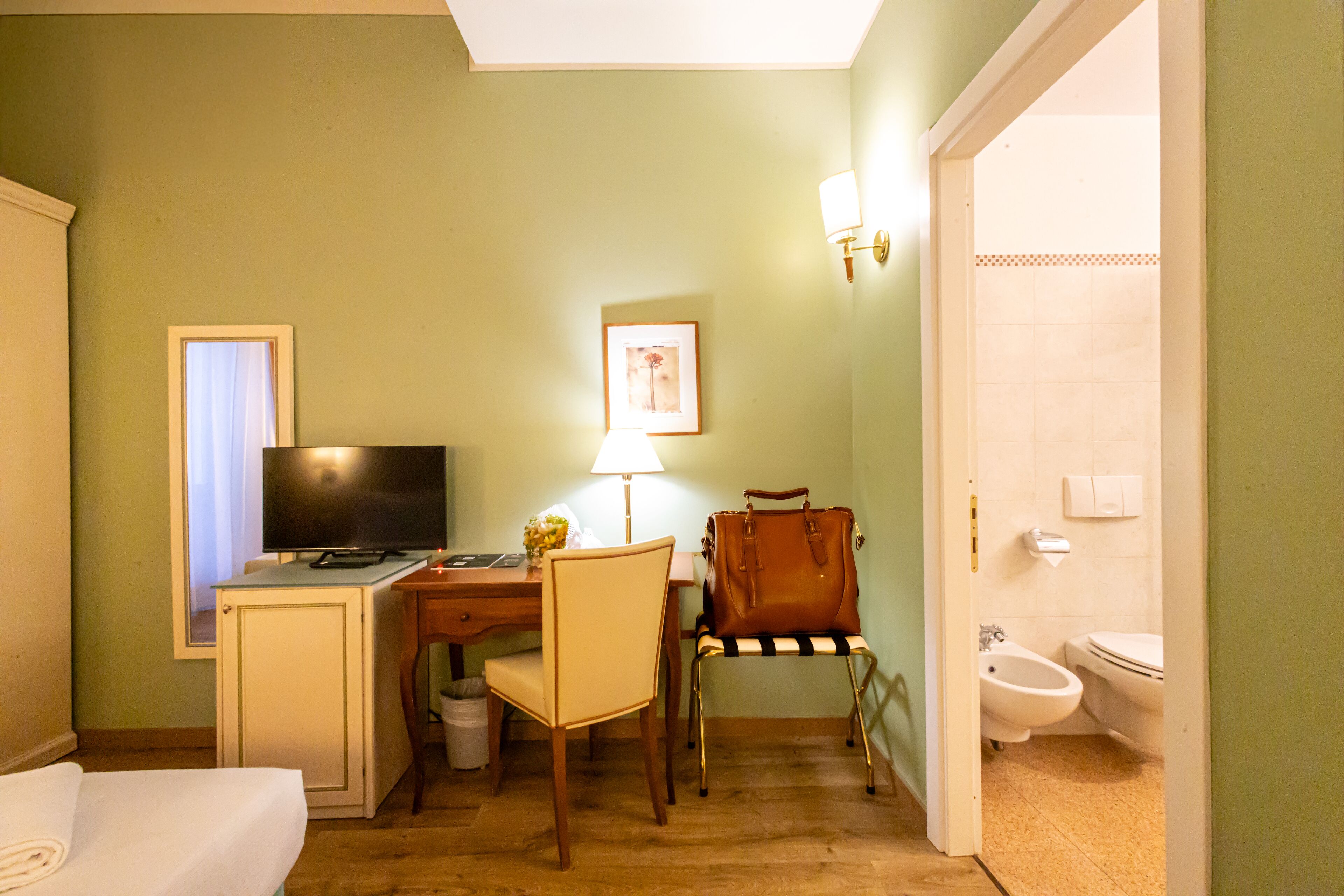 A hotel room with a bed, desk, chair, television, lamp, and a bathroom with a toilet and bidet.