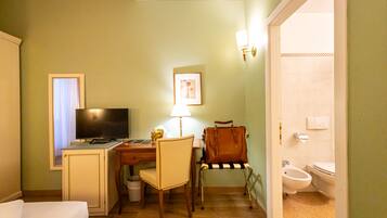 A hotel room with a bed, desk, chair, television, lamp, and a bathroom with a toilet and bidet.