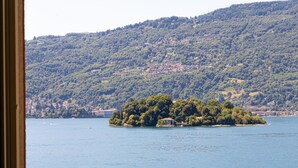 Vista de un lago con una pequeña isla, un pueblo lejano y un balcón con barandilla y flores.