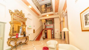 Un amplio vestíbulo con un espejo grande y ornamentado, una escalera y un objeto cilíndrico rojo en el suelo.