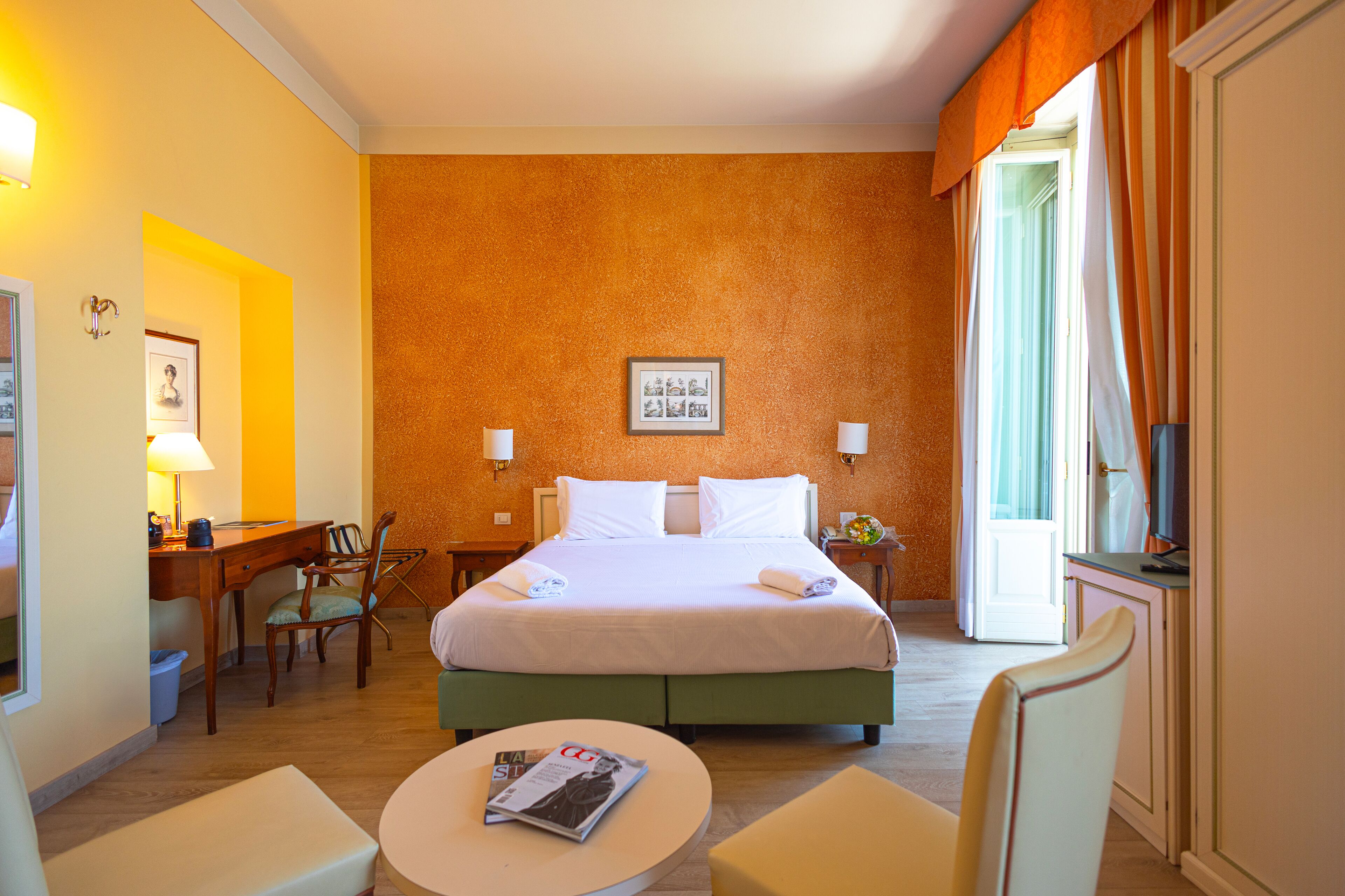 A hotel room with a bed, bedside tables, a desk, a chair, and a round table with a magazine.
