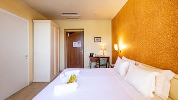 A hotel room with a neatly made bed, a desk with a chair, and a door leading to another room.