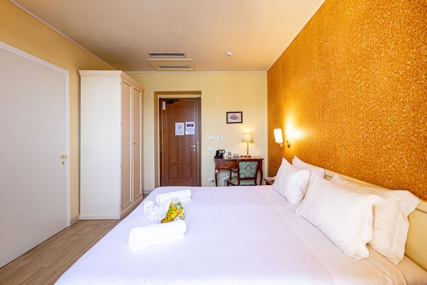 A hotel room with a neatly made bed, a desk with a chair, and a door leading to another room. - LVG Hotel Collection - Pallanza (Verbania)