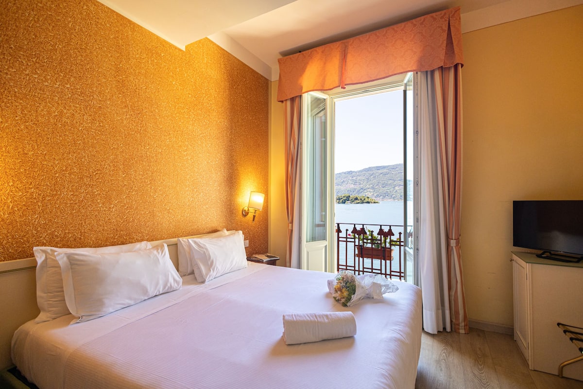 A hotel room with a large bed, a television, and a balcony with a view of the water.