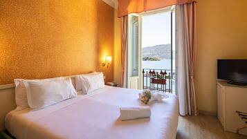 Habitación de hotel con una cama grande, televisión y balcón con vista al agua.