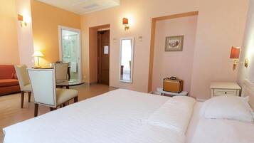 Une chambre d’hôtel avec un grand lit, un bureau avec une chaise, une petite table, une valise et une table de chevet.