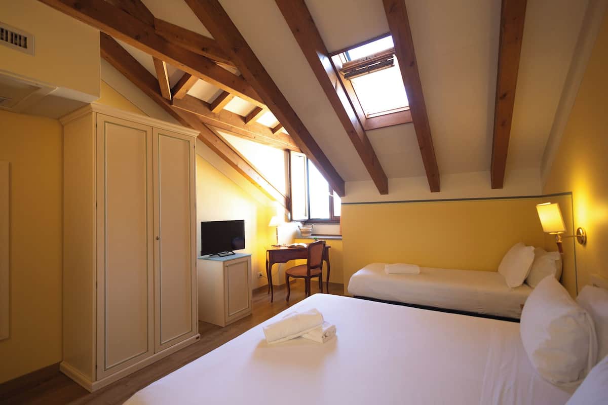 A bedroom with a bed, a desk with a television, and a window.