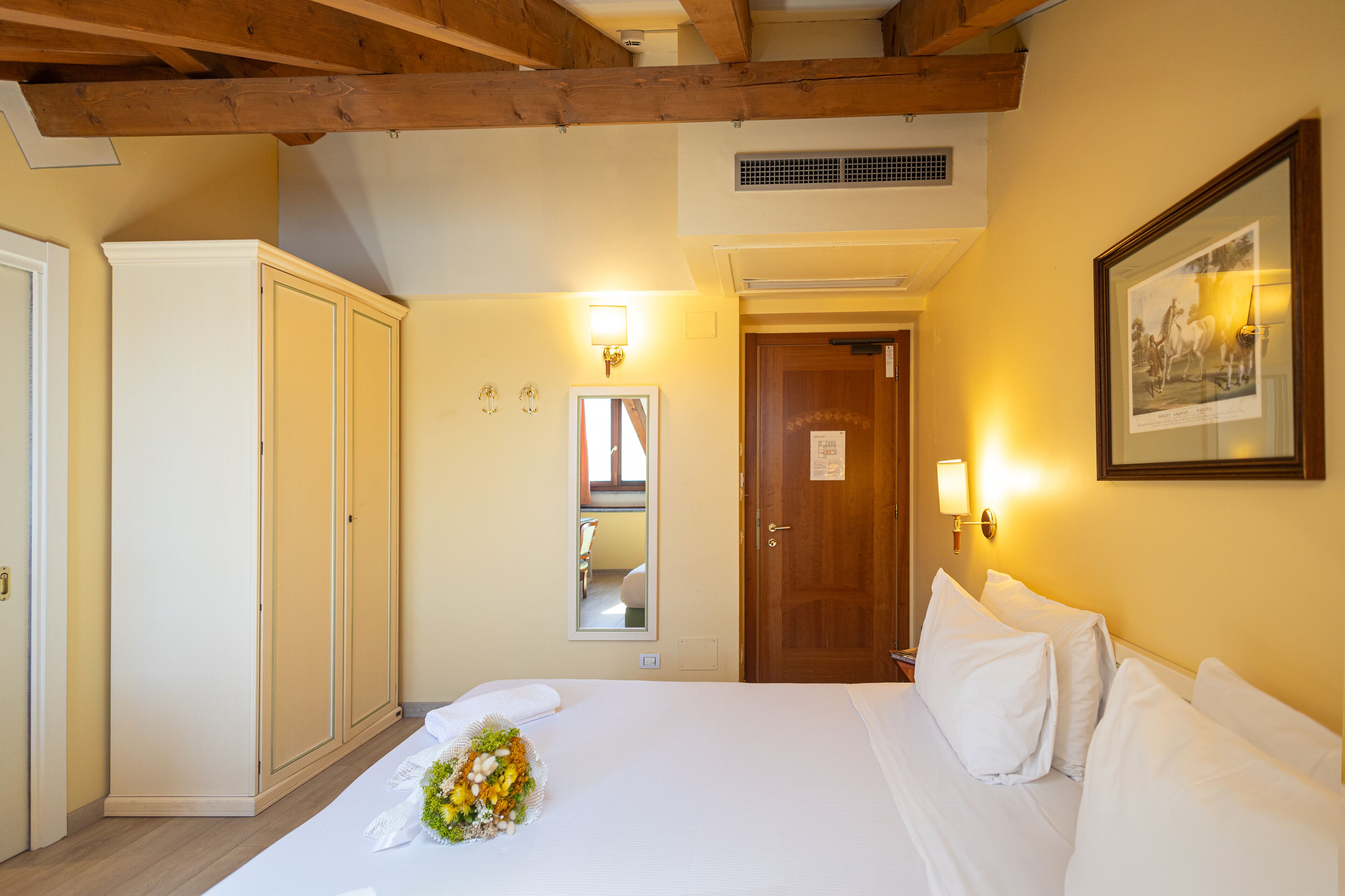 Quarto de hotel com teto de madeira, cama com roupa de cama branca, espelho e quadro na parede.