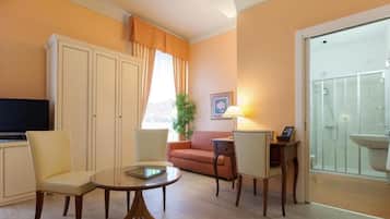Sala de estar com sofá, cadeiras, mesa de centro, televisão e banheiro com pia e chuveiro.
