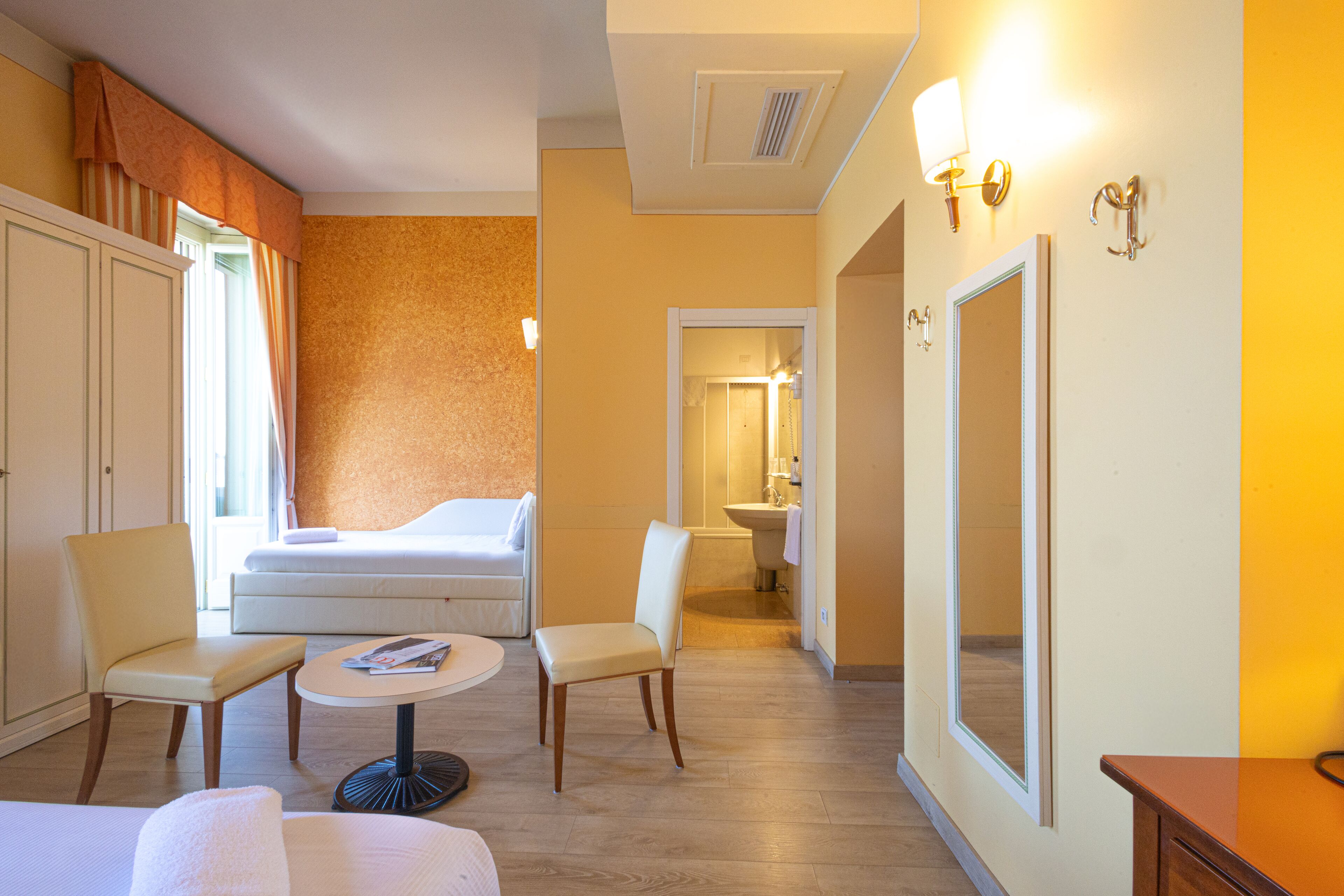 A hotel room with a bed, two chairs, a round table, a mirror, and a bathroom visible through an open door.