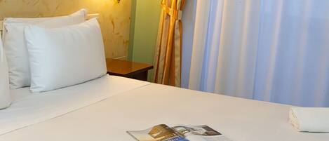 Habitación de hotel con cama, almohadas, mesita de noche, lámpara y una revista sobre la cama.