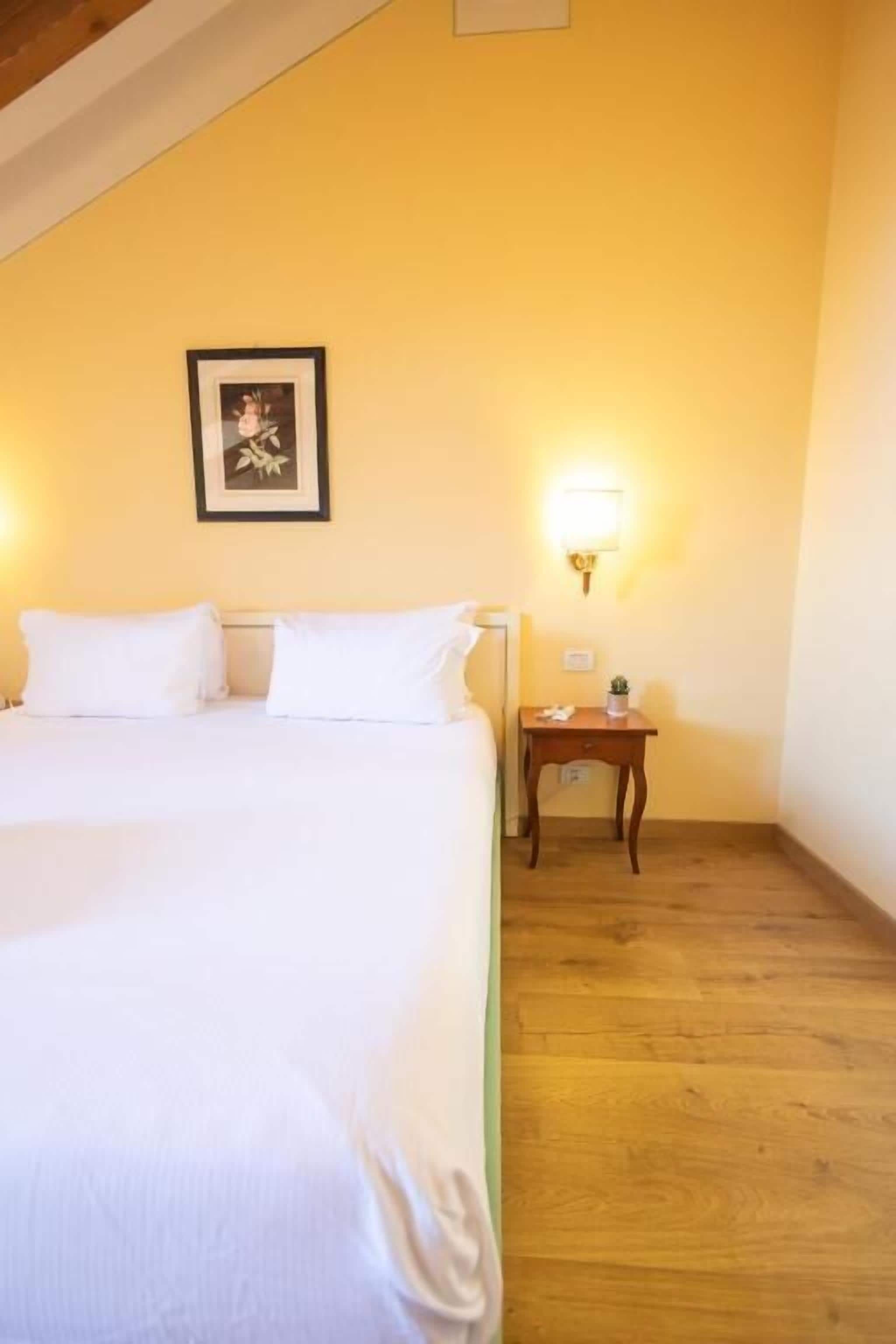 Habitación de hotel con una cama, una mesita de noche, una lámpara de pared y un cuadro enmarcado.