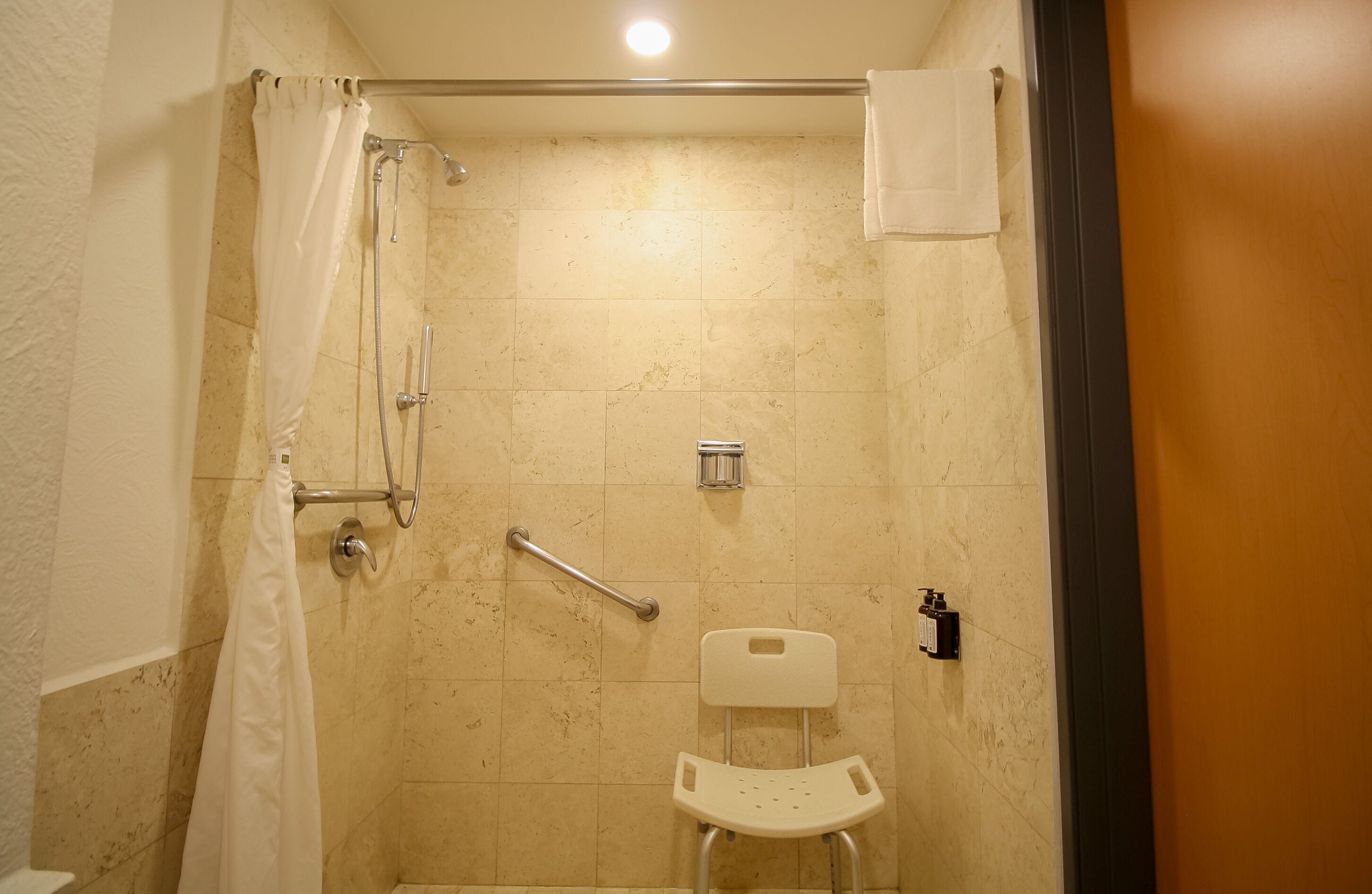 Une cabine de douche équipée d’une barre d’appui, d’une chaise blanche et d’un porte-serviettes.