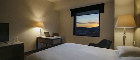 Habitación de hotel con cama, escritorio, silla, televisor y ventana con vistas.