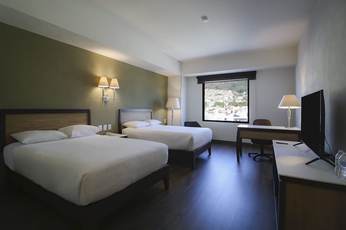 A hotel room with two beds, a desk, a TV, and a window with a view.