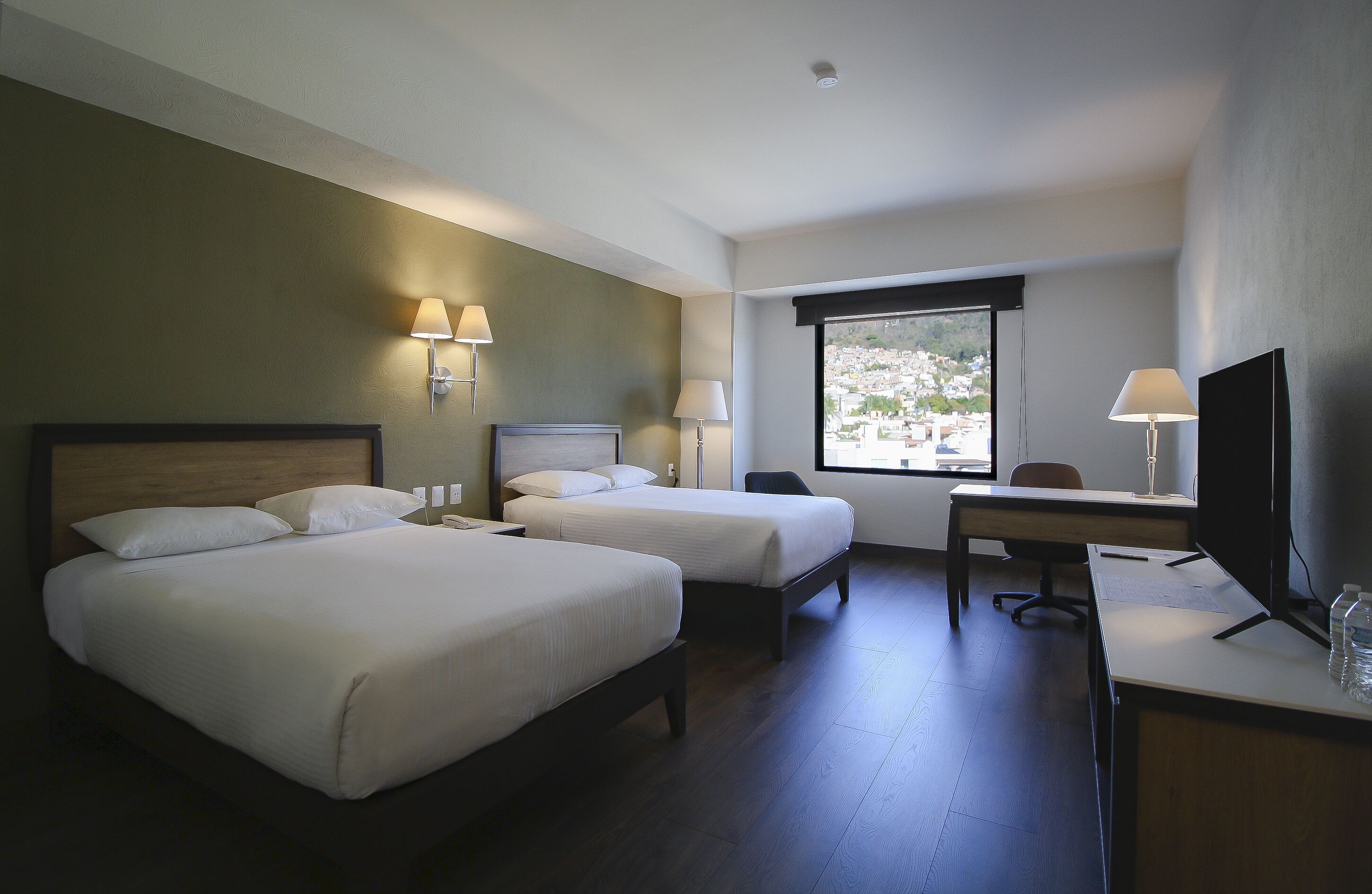 A hotel room with two beds, a desk, a TV, and a window with a view.