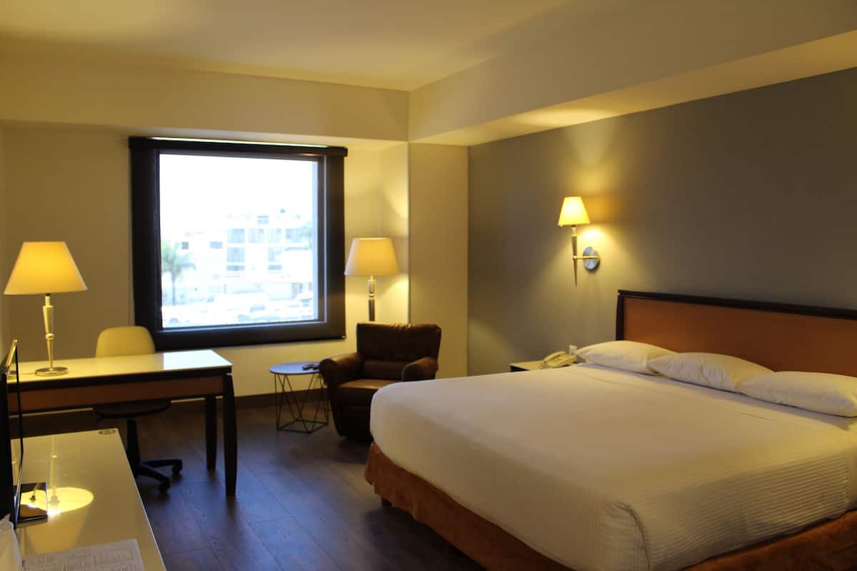 A hotel room with a bed, desk, chair, two lamps, and a window.