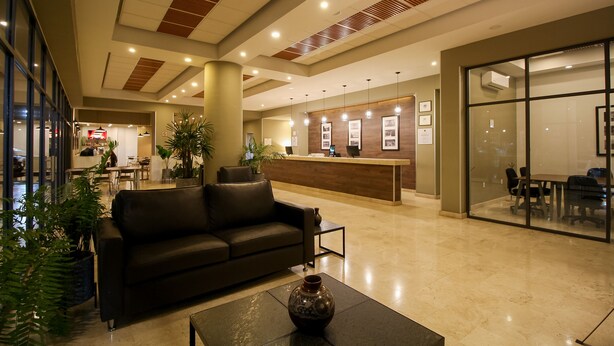 A hotel lobby with a reception desk, a sofa, a coffee table, and potted plants. - Turotel Morelia (Morelia)