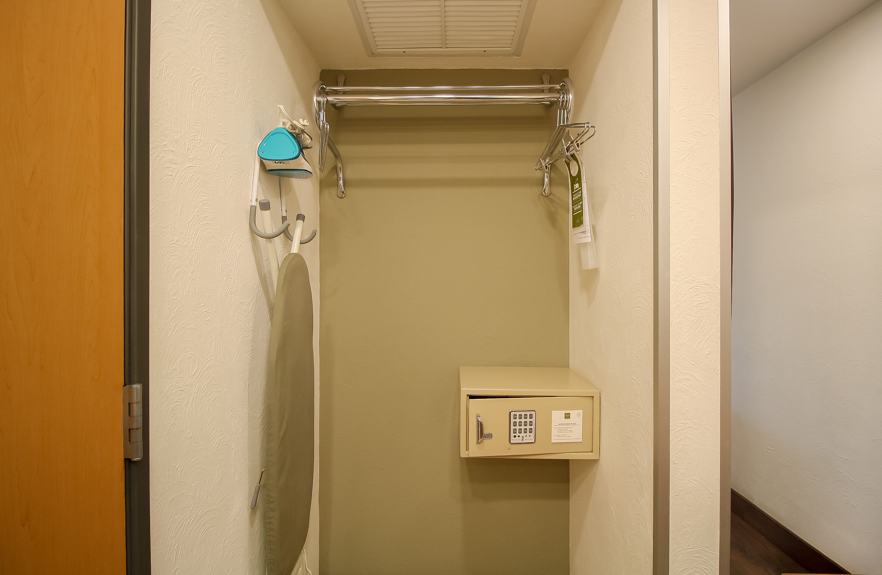 A narrow hallway with a wooden door, a towel rack, a towel dispenser, and a small utility cabinet.