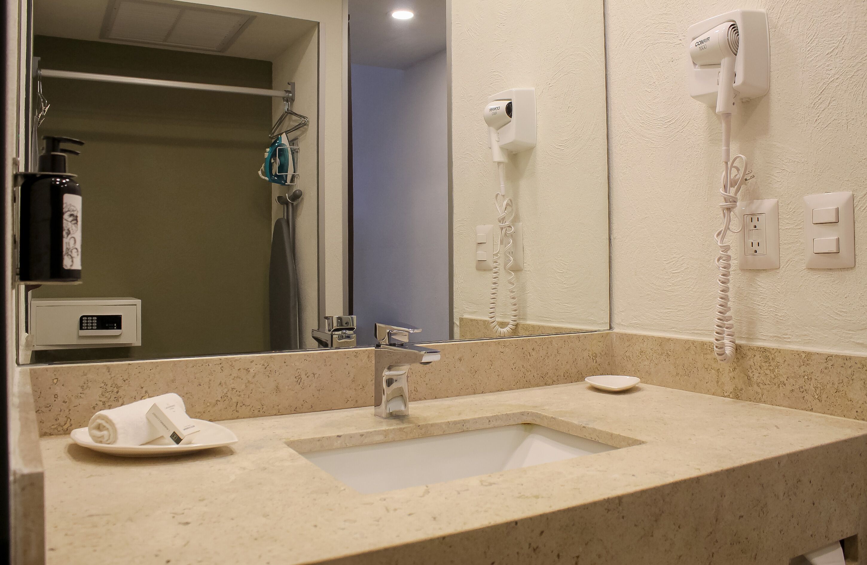 A hotel bathroom with a sink, mirror, hair dryer, and a towel on the counter.