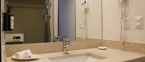 Un baño de hotel con lavamanos, espejo, secador de pelo y una toalla sobre la encimera.