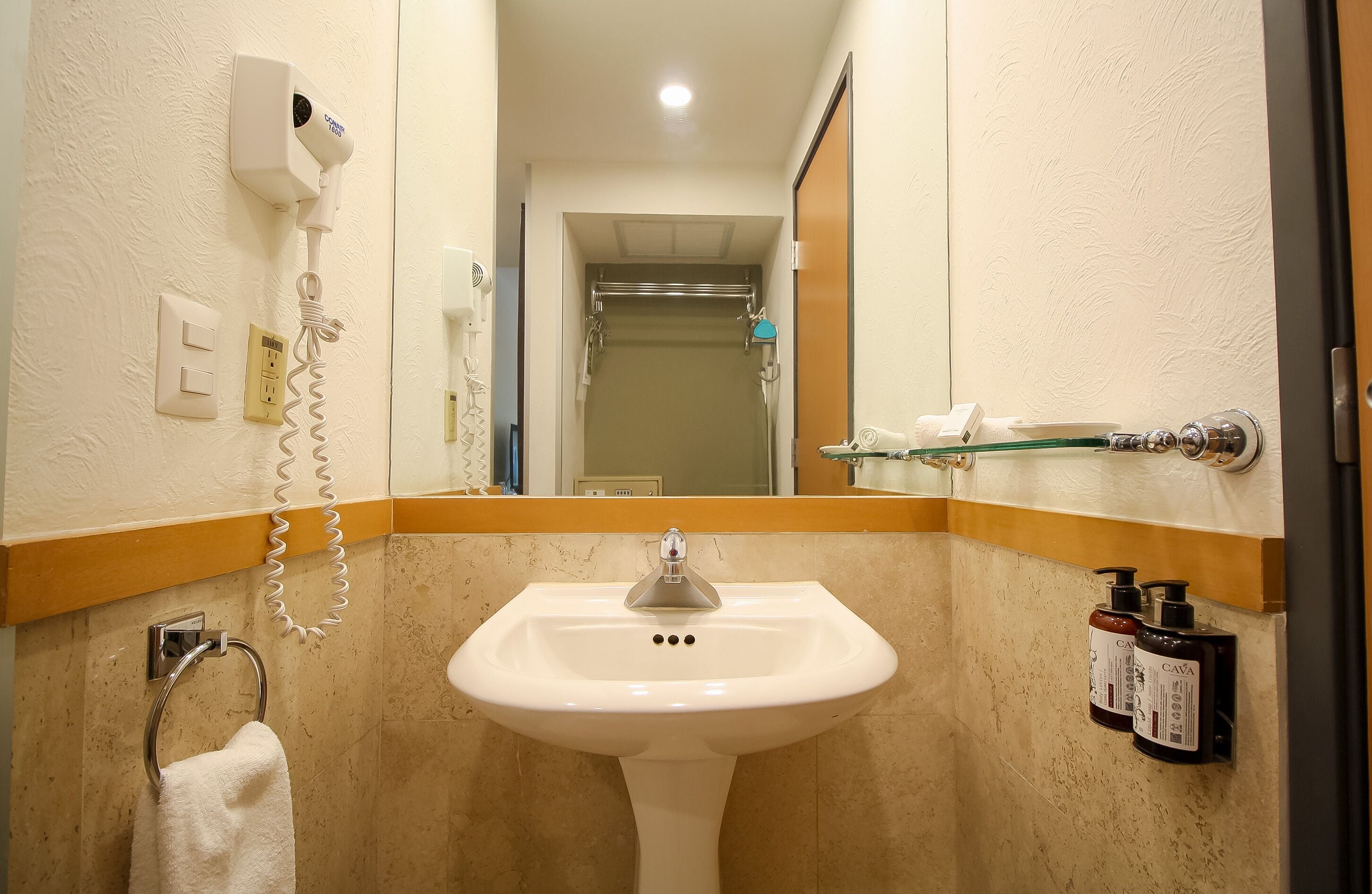 Un baño con lavamanos, perchero para toallas, secador de manos y espejo.