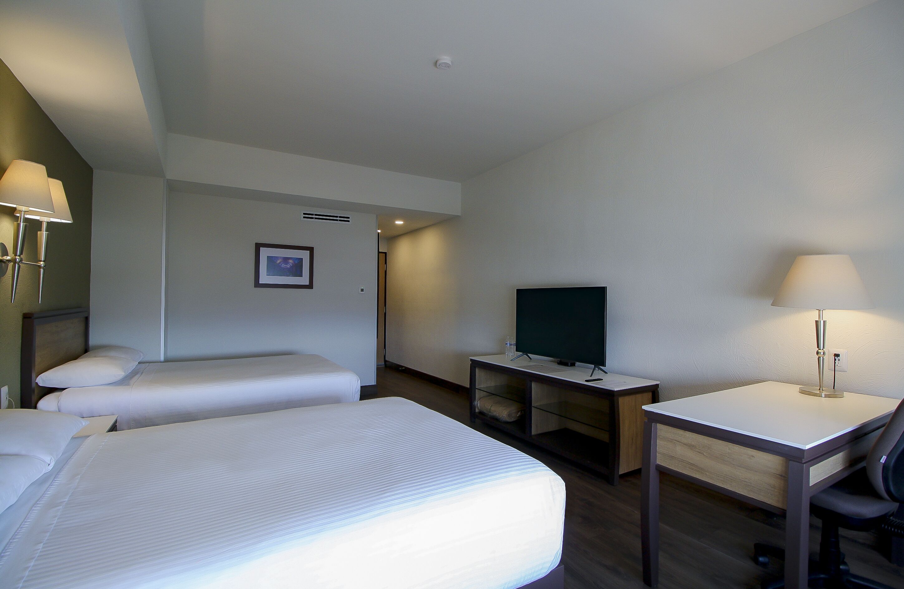 A hotel room with two beds, a desk, a chair, a television, and a lamp.