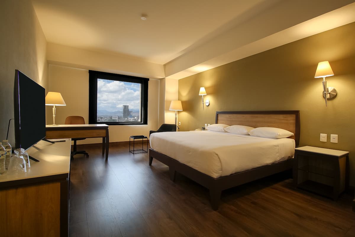 A hotel room with a bed, desk, chair, and a television.