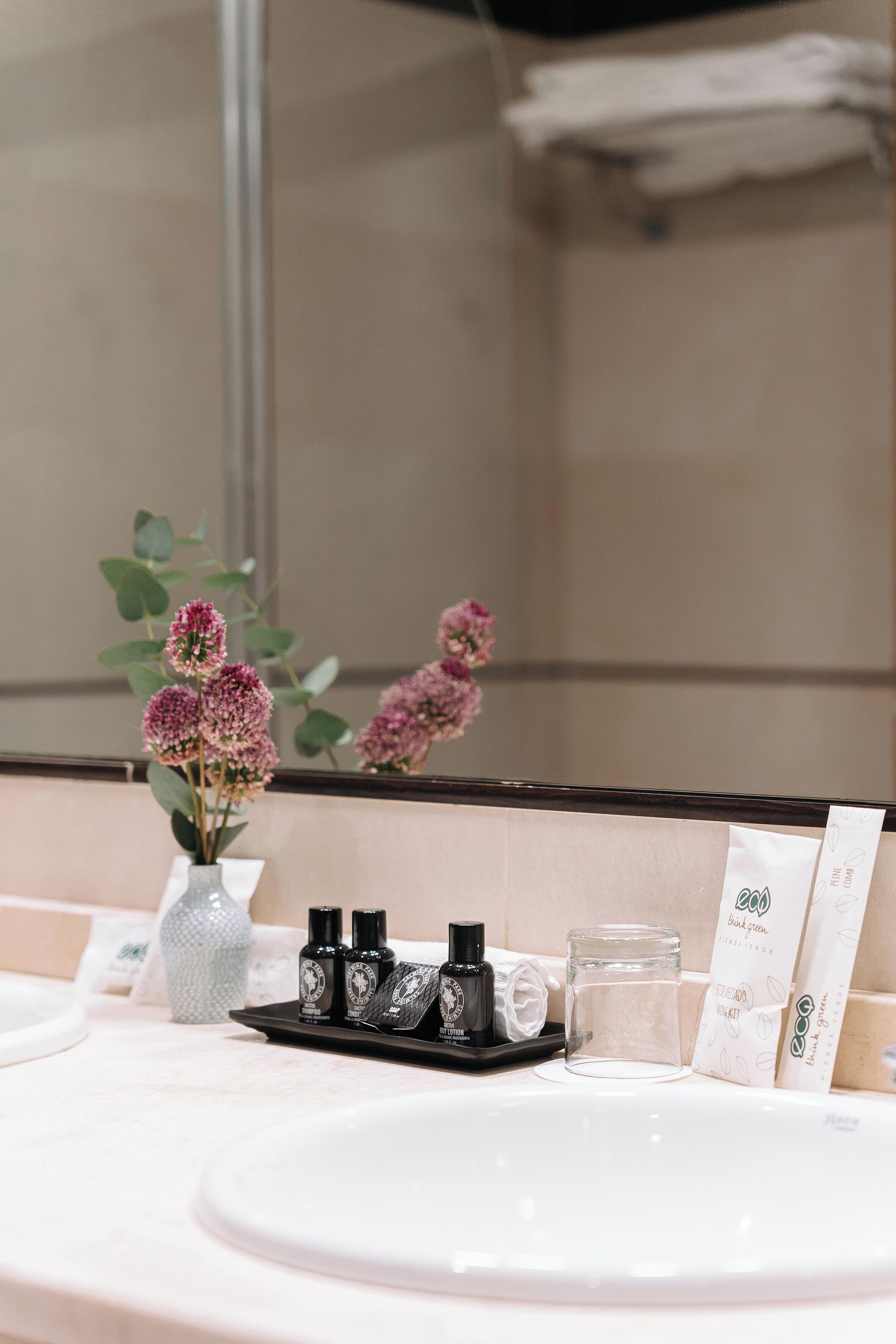 A bathroom vanity with a white sink, a vase with flowers, and various toiletries.