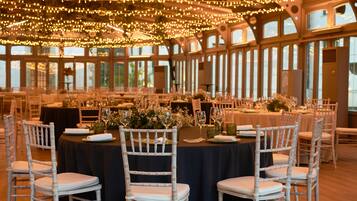 A banquet hall with round tables, white chairs, and string lights.