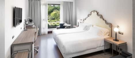 A hotel room with a large bed, a desk, a chair, a TV, and a view of a garden.