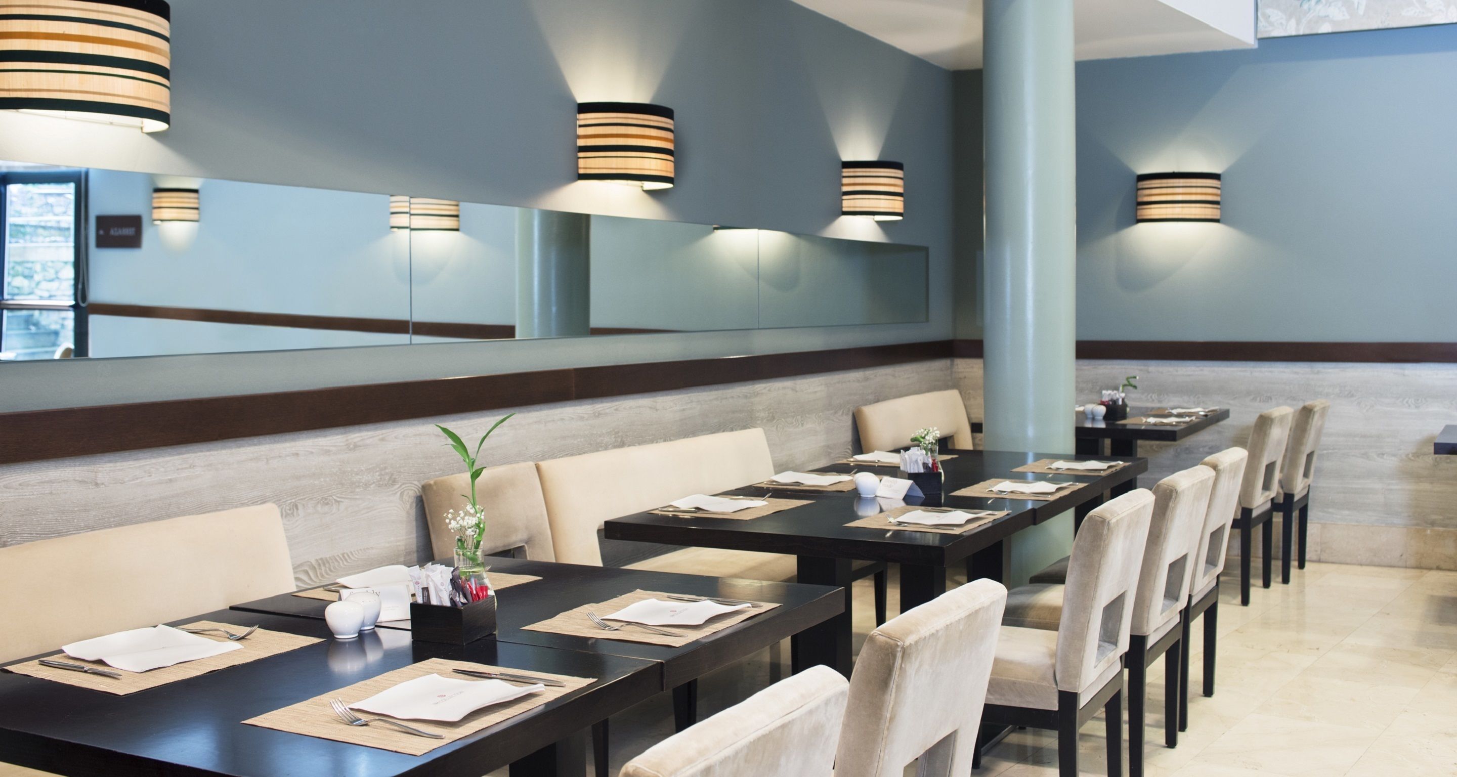 A restaurant with long tables, chairs, and modern pendant lighting.