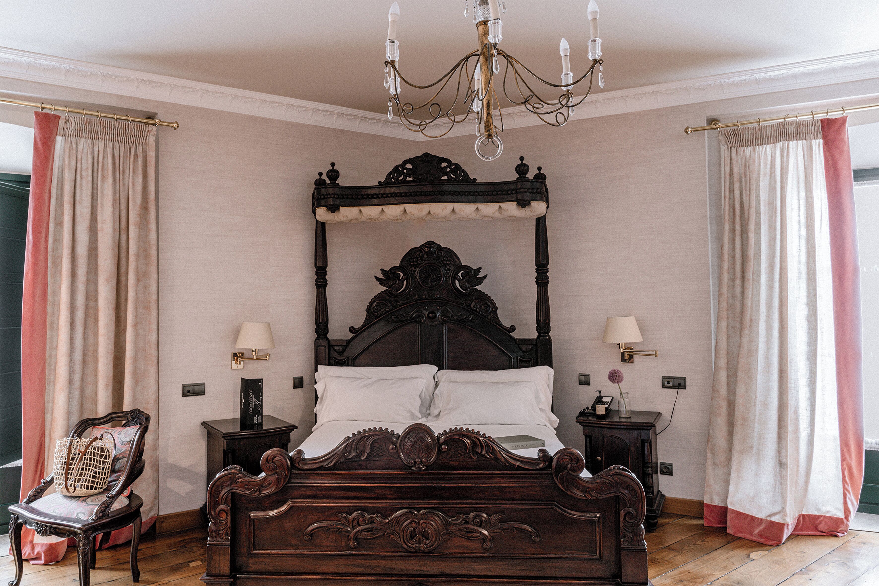 Un dormitorio con una cama grande y ornamentada, dos mesitas de noche con lámparas, una silla y un candelabro.